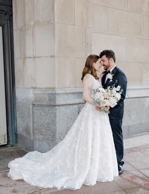My husband and I are standing outside of the hotel, face to face with our noses touching. We're smiling and very happy because we're about to get married.