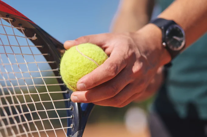 A close-up of a person serving a tennis ball.