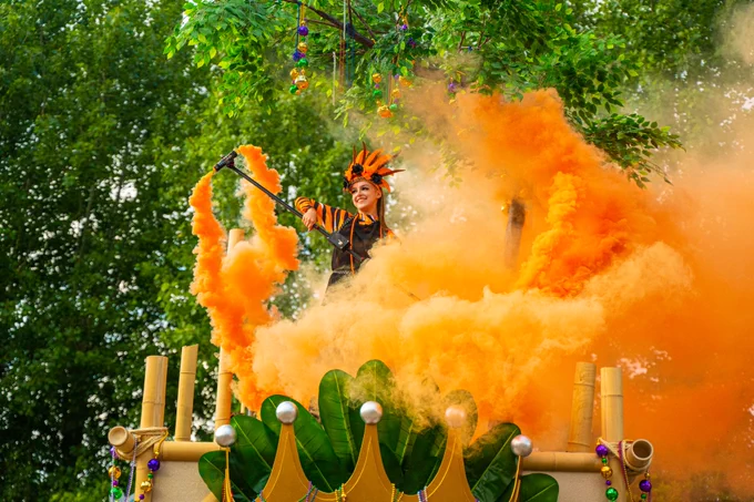 A member of the Clawsome Krewe wearing a tiger striped party outfit on their Krewe stage. They are holding a baton with bright orange smoke surrounding them