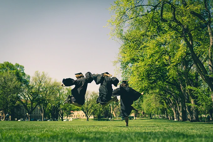 Students in graduation regalia jump for joy at Colorado State University's Oval. 