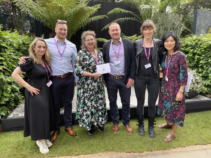 Photo of Rosemary, Coldstream with her team, and LandDesigns Ltd. Smiling in front of the feels like home garden at Chelsea Flower Show with a gold medal lush tree ferns in the background.