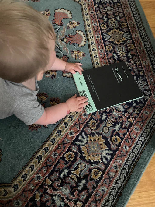 my baby’s chubby hands holding the green and black Canadian version of gravitas on a floral rug