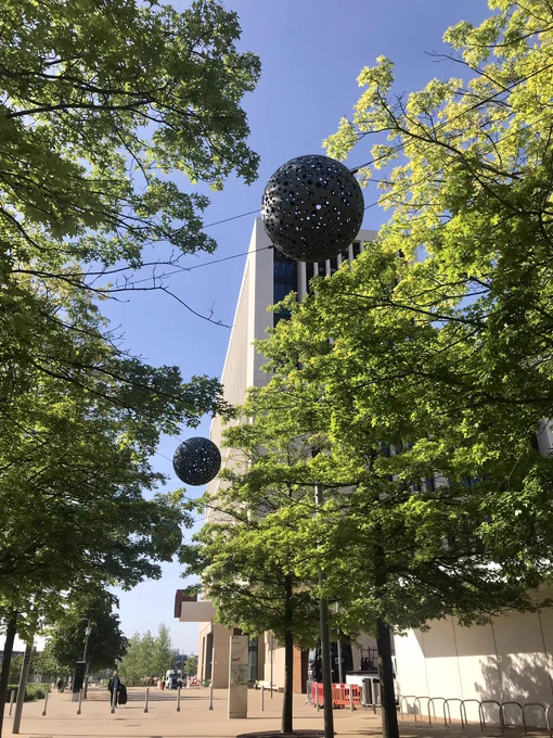 Trees with silver sphere ornaments hanging along a wide path leading to UCL’s Marshgate building