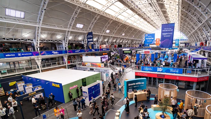 the photo shows the main exhibition and show floor at The Podcast Show 2023 - with the sun shinning in from the windows - people are filling up the space and walking around between the stands