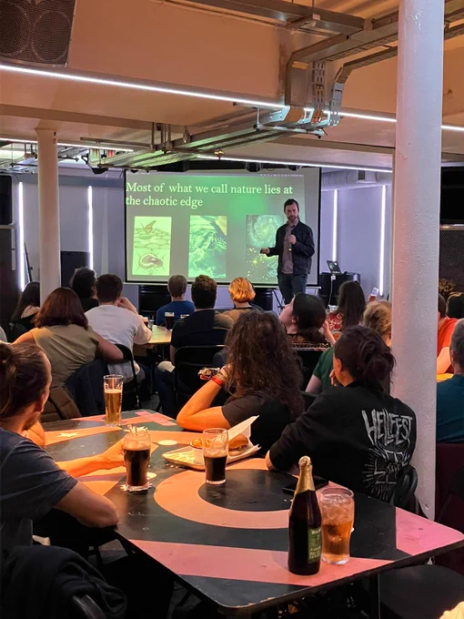 One of our speakers on stage with a presentation slide saying "Most of what we call nature lies at the chaotic edge", talking to our audience