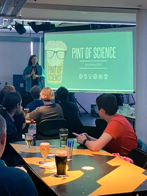 Me, standing on a stage in front of a Pint of Science screen, speaking to our audience