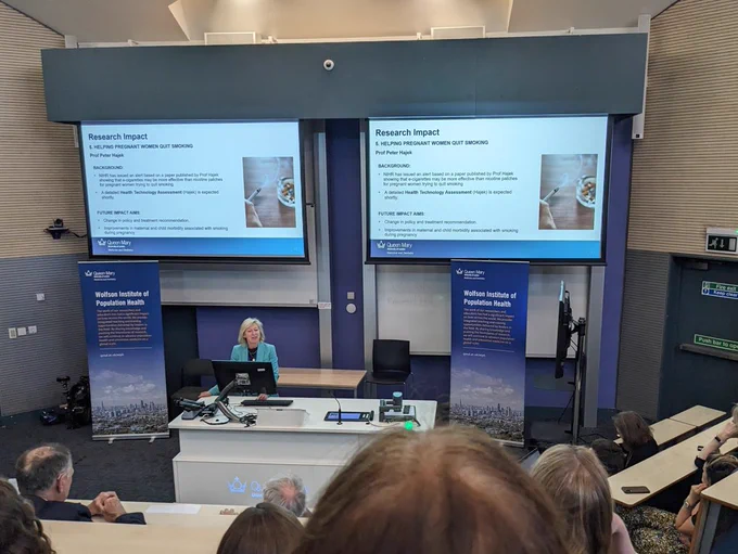 Picture of presentation taking place in lecture theatre, with slides showcasing impact of Peter Hajek's research into smoking cessation during pregnancy