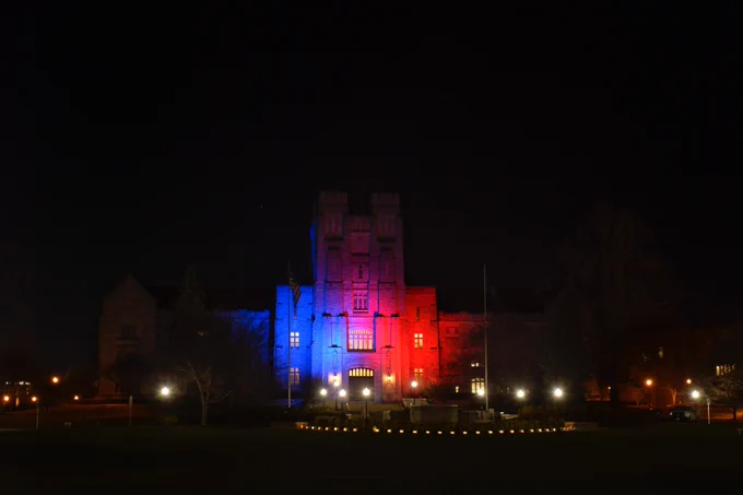 Burruss Hall illuminated red and blue at nighttime, with one side of the building illuminated blue and the other red.