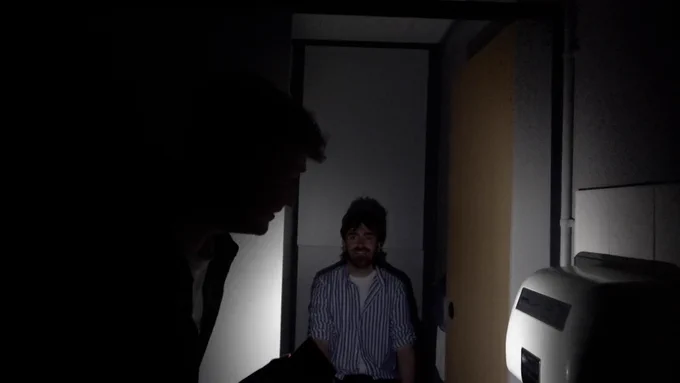 Daf creeps around in a bathroom with the lights off holding a torch. Luke peers creepily out of a stall.