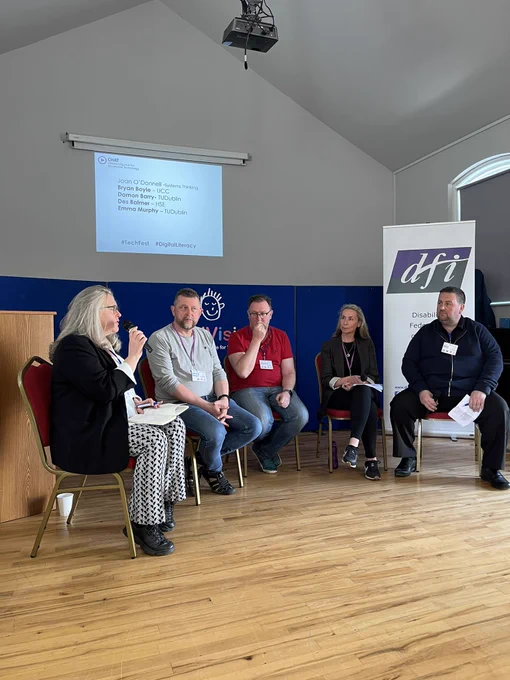Five people on a panel discussion at the top of a room.