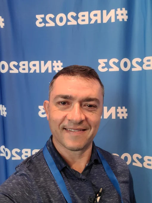 Anthony smiles in front of a blue #NRB2023 backdrop.