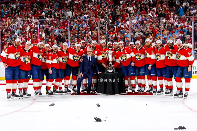 The Florida Panthers posing for a photo with the Prince of Wales trophy on ice in Panthers home uniforms.