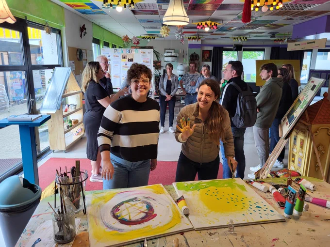 Dues de les participants en una de les visites a una entitat on treballen l'art com eina terapèutica i de lleure. Se les veu a davant de dos quadres i pintant amb les mans.