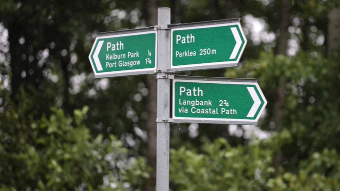 metal sign pole with three green 'path' signs pointing in different directions with white writing.  Trees in the background.
