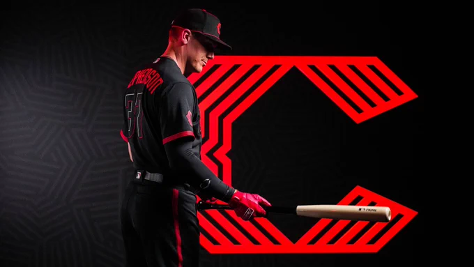 Tyler Stephenson looks down at a bat while wearing the Reds new City Connect uniforms. 