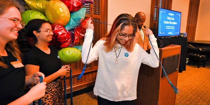 A student celebrates their graduation at the First Gen ceremony. They're holding a blue cord around their shoulders.