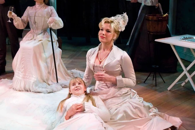 A photo showing Hannah Waddingham and a young actress sat on a stage staring into the middle distance in victorian clothing 