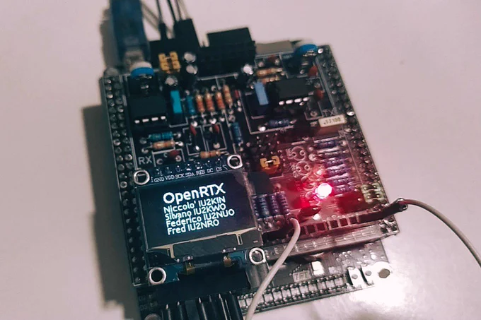 Picture of BB Hat, an add-on for the STM32 Black Board that includes a display and keys, that show the OpenRTX about screen, as well as all the passives needed to interface with an analog radio. A red LED is lit on the board.