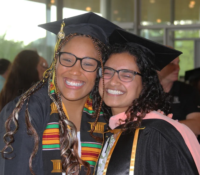 2 female students in cap and gown hugging and smiling.