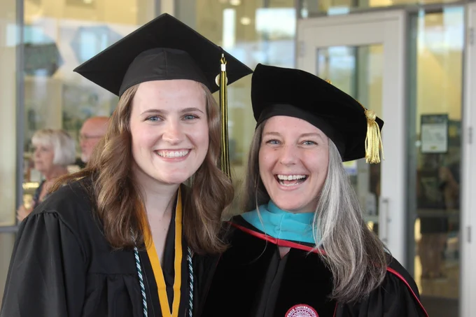 2 females in graduation cap and gown smiling for the camera.