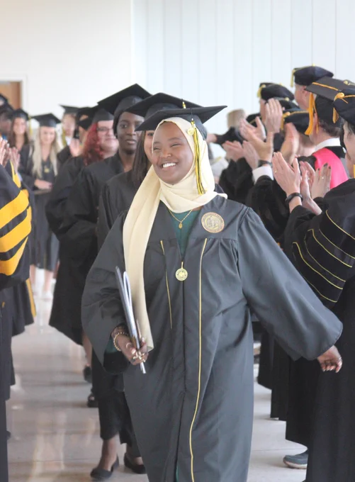 Student in graduation cap and gown walking toward the camera and smiling.