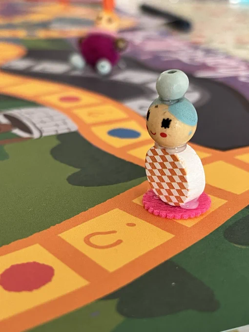 A playing piece on a board game. The piece is made of three beads glued together to look like a body, a head and a hair bun