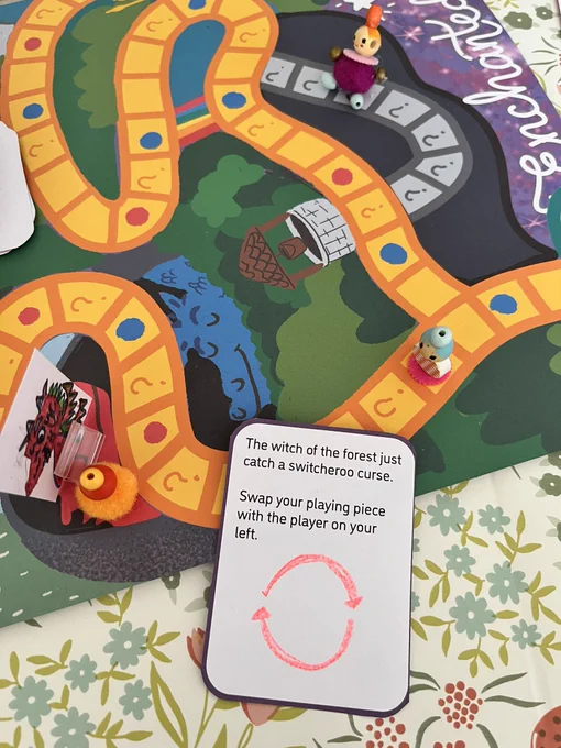 A picture of the playing board and a mystery cards that reads “the witch of the forest just cast a switcheroo curse, swap your playing piece with the player on your left”