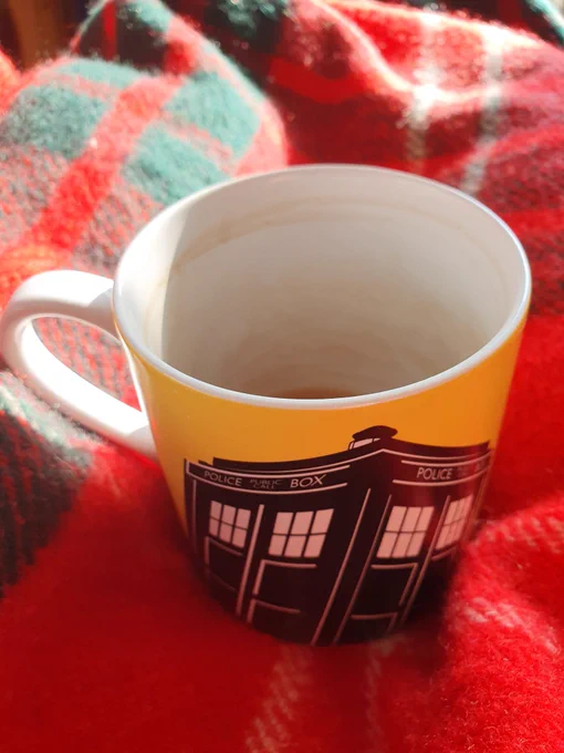 A yellow mug with the tardis on sitting on a red blanket. 