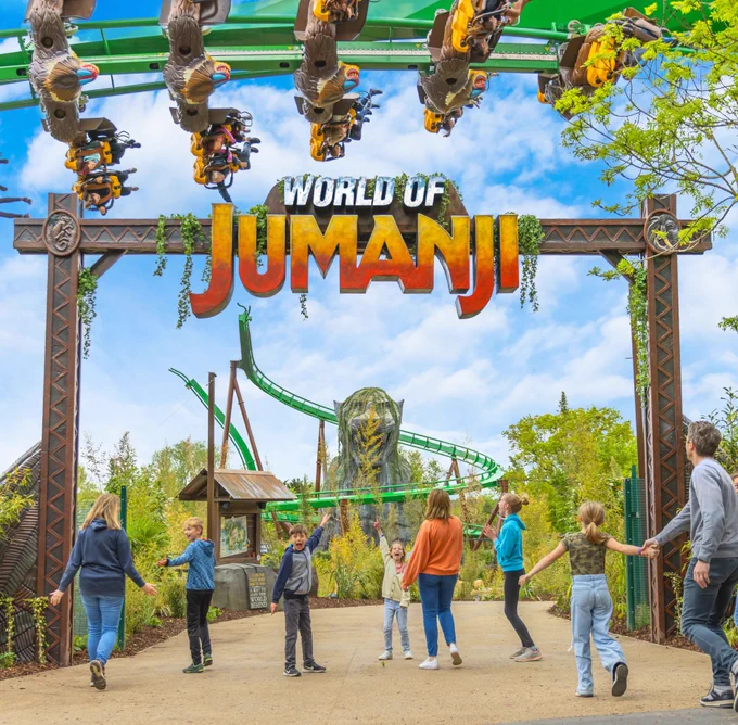 Families entering the World of Jumanji whilst rollercoaster, Mandrill Mayhem, flies above them with an inversion