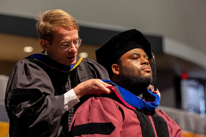 A man looking confidently and proudly ahead as he is hooded during the ceremony.