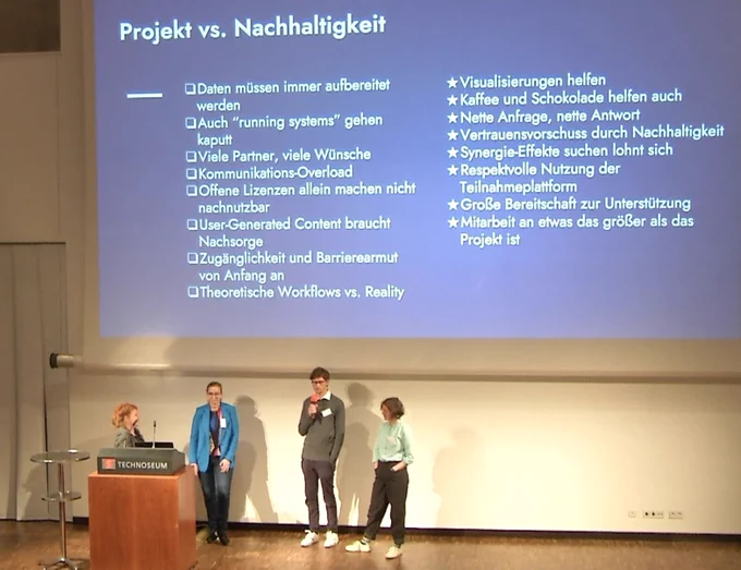 Screenshot: Die vier Vortragenden auf dem Podium des Technoseums, dahinter die Slide “Learnings: Projekt vs. Nachhaltigkeit”
