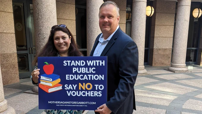 Zeph Capo and Nancy Thompson hold up a sign that says "Stand with public education. Say no to vouchers."