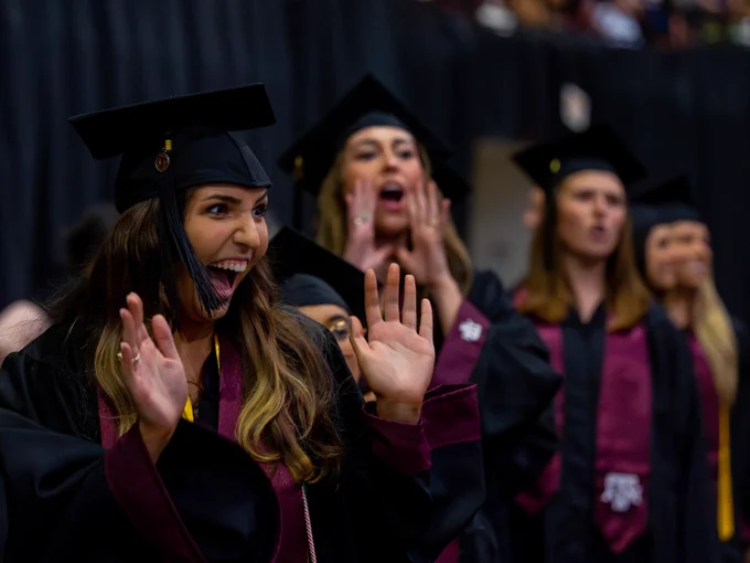Graduates yelling and looking happy on the floor of the ceremony.