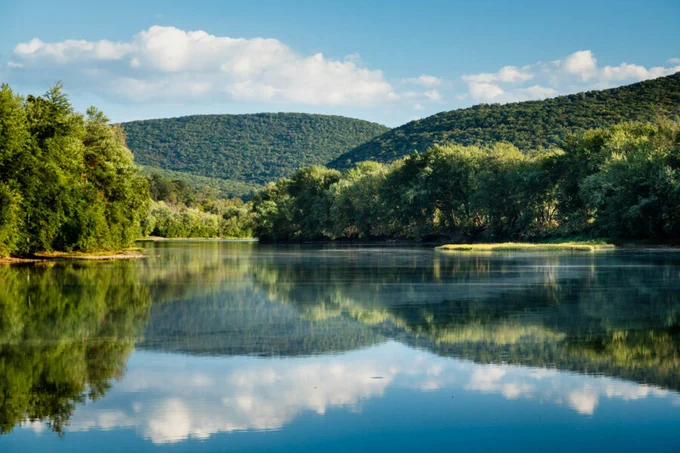 Mountains, trees, and a blue sky with clouds reflect in the waters of the Susquehanna River in PA
