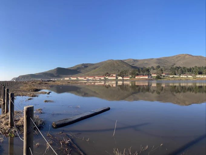 a series of photos of the Rodeo Lagoon taken about 24 hours apart. The before photos show a high-water line up the protective fence in some locations. The after photos show a drop in the water level, and a starkly receded shoreline revealing about 15 feet of dirt and dried grass. In all the photos you can see the rows of old army barracks making up Fort Cronkhite, and rocky, shrub covered hills in the background.