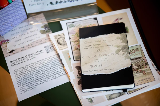 A book titled "Queer Desire at Smith College: A collaborative mem book" rests atop floral images and a card describing the project by Isabel Aragon '23.