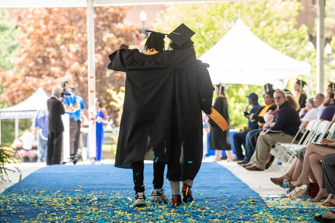 Two graduates walk off arm in arm after a commencement ceremony. 