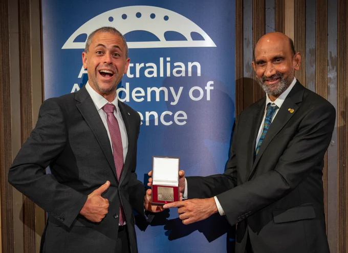 A man grins widely as he receives  medal from another man. 