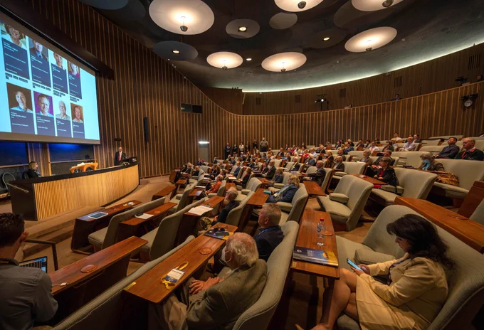 A large group of people sit inside an amphitheatre. 