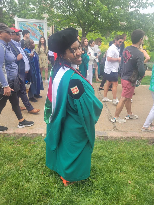 Black woman wearing a Tam, green graduation gown, and green hood