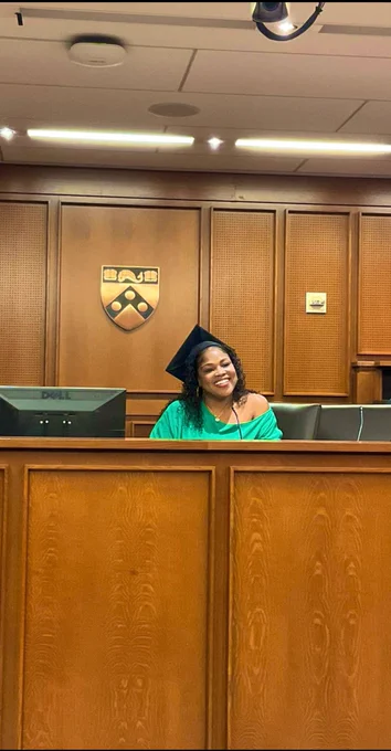 Tonya Bennett sitting on a judges bench in a courtroom. She is smiling wearing a green dress and a graduation cap.