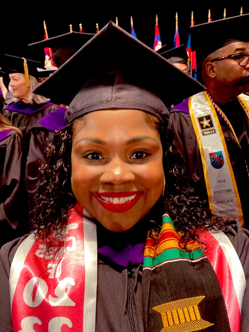 Tonya Bennet on the stage at the Penn Law graduation ceremony , She is smiling wearing a cap and gown and a pink and grey honor stole the second honor stole is red black and green.