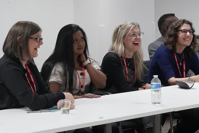 Female board members sat in a row and smiling at a desk. 