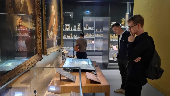 Iain and Nick reading a display panel in the new Hunterian Museum. On the left-hand wall hang portraits of John Hunter and his brother William. In the background is another visitor looking at shelves full of glass specimen jars, which continue into the next gallery. 