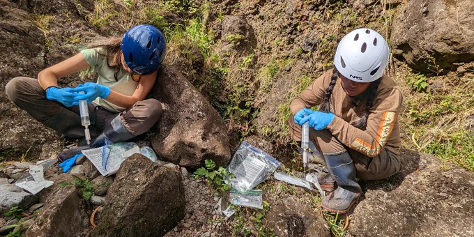 Two USGS scientists sampling eDNA from a rock pool along the Puka Stream in Hawaii