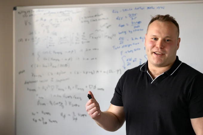 Person standing in front of a whilte board covered in cryptic mathematica writing