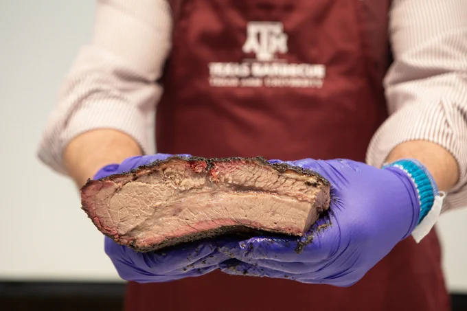 gentleman in a maroon and white apron holding freshly cooked brisket