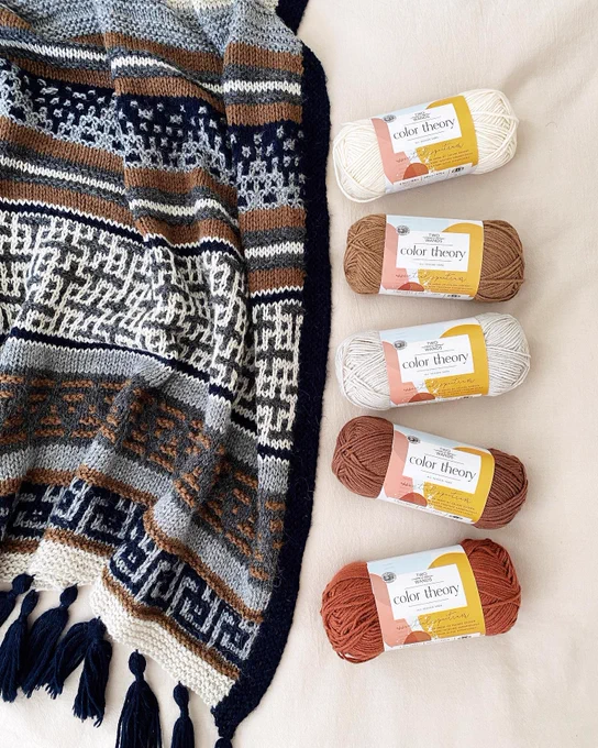knit blanket with creative pattern next to skeins of yarn
