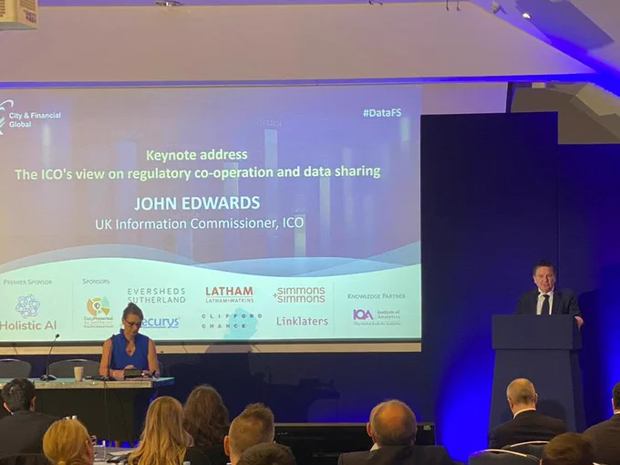 John Edwards is on the stage behind a lectern delivering a keynote speech. There's a  screen behind John that says, " Keynote address The ICO's view on regulatory co-operation and data sharing. John Edwards UK Information Commissioner, ICO" 