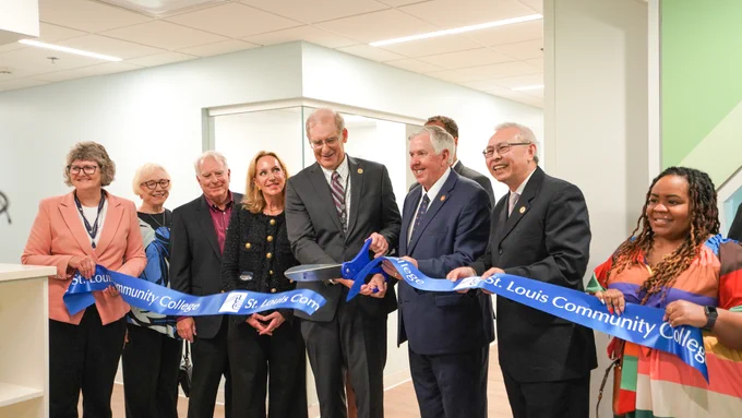 Jeff Pittman, Ed.D., chancellor of STLCC and Governor Mike Parson cut a blue STLCC ribbon with a large pair of scissors. Multiple people stand besides them and hold the ribbon, smiling.